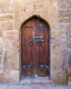 The sturdy wooden door at Ateshgah Fire Temple showcases intricate metal hardware against the backdrop of ancient stone walls. Sunlight highlights its historical significance