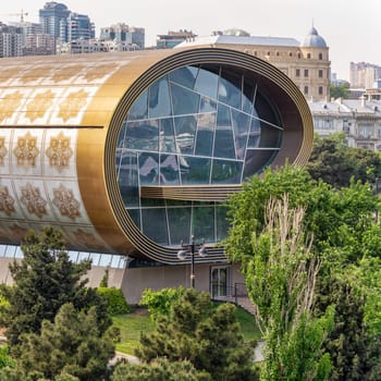 Side view of the Carpet Museum in Baku, Azerbaijan showcases its striking modern architecture, featuring a curved golden big window, nestled among lush greenery