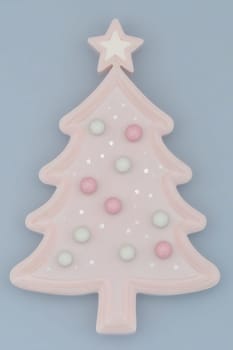 A pastel Christmas tree shaped decoration adorned with colorful polka dots rests against a soft blue backdrop, creating a festive vibe.