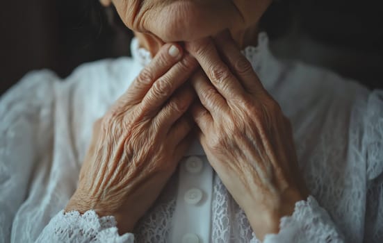 An elderly woman with delicate hands cradles her throat, reflecting a moment of tenderness and introspection in a cozy indoor setting.
