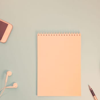Creative flat lay photo of workspace desk with paper notebook, smartphone, earpieces, pen and coffee with copy space background minimal style