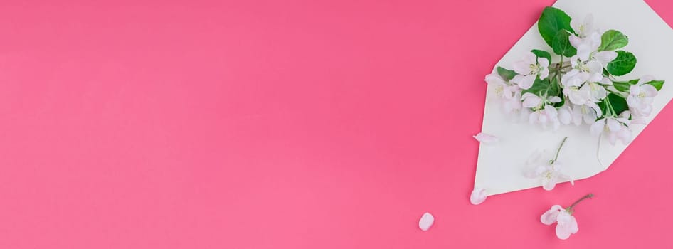 Creative flat lay long wide banner of blank letter envelope and apple tree flowers on millennial pink background with copy space in minimal style, template for celebration, invitation, valentine cards