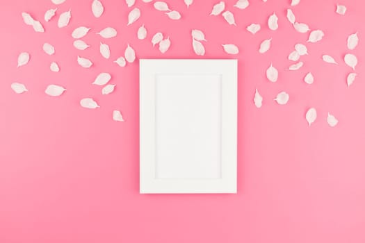 Creative flat lay concept top view of white frame mock up and apple tree flowers petals on pastel pink background with copy space in minimal style, template for text