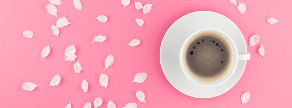 Creative flat lay concept top view of coffee cup and white apple tree flowers petals on pastel pink background with copy space in minimal style, long wide banner