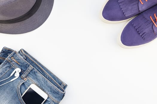 Flat lay of suede shoes, blue jeans, grey hat, cactus and smartphone with headphones on white background with copy space. Overhead view of woman casual outfit. Trendy hipster look top view