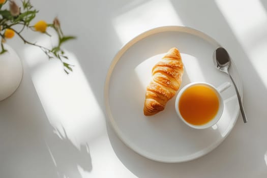 A serene breakfast tray displays a warm croissant next to a cup of tea, set against a bright surface illuminated by gentle morning light, creating a calming atmosphere.