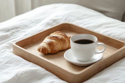A simple breakfast tray features a freshly baked croissant and a steaming cup of coffee, set against a soft, white bedspread. The scene evokes a sense of calm and relaxation to start the day.