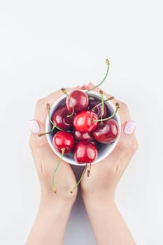 Creative top view of fresh ripe cherry in a bowl with hands and copy space isolated on white background minimal style. Concept of summer fun and healthy eating. Template for your text or food design