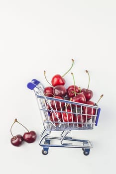Creative image of ripe cherries in a shopping cart with copy space isolated on white background in minimal style. Concept of supermarket or fruit market shopping. Template for your text or design.