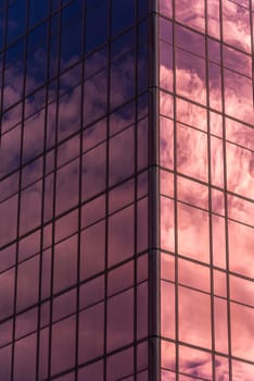 Sky and clouds reflected in windows of pink modern office building