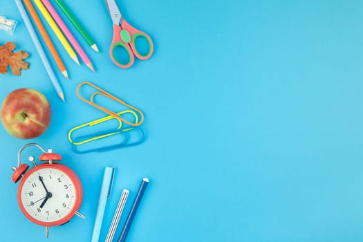 Creative flat lay top view back to school concept with alarm clock, color school and office supplies on bright turquoise paper table frame background with copy space, template for text or design