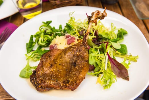 Dish with a roasted duck leg and green salad on a white plate