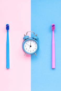 Teeth hygiene and oral dental care products and alarm clock on color pink and blue background with copy space. Toothbrushes Flat lay, top view composition, Morning concept
