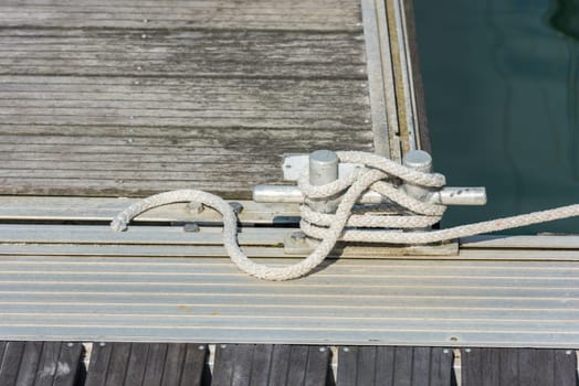 Mooring rope with a knotted end tied around a cleat on a wooden pier