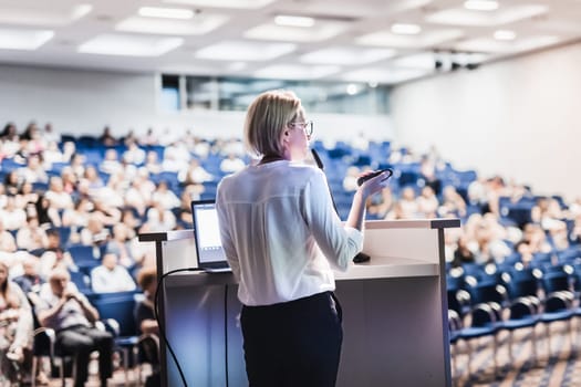 Female speaker giving a talk on corporate business conference. Unrecognizable people in audience at conference hall. Business and Entrepreneurship event