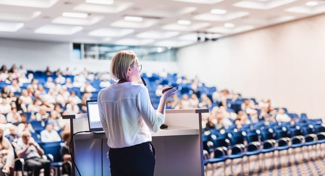 Female speaker giving a talk on corporate business conference. Unrecognizable people in audience at conference hall. Business and Entrepreneurship event