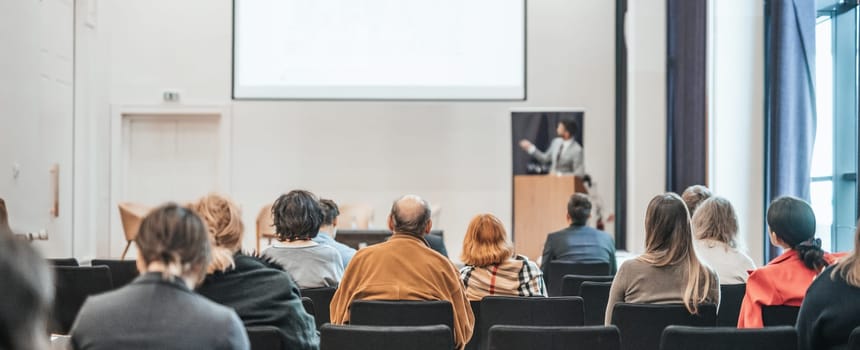 Speaker giving a talk in conference hall at business event. Rear view of unrecognizable people in audience at the conference hall. Business and entrepreneurship concept
