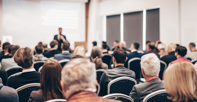 Speaker giving a talk in conference hall at business event. Rear view of unrecognizable people in audience at the conference hall. Business and entrepreneurship concept
