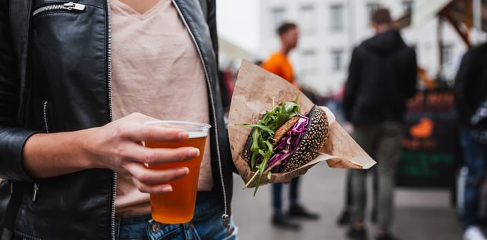 Close up of woman hands holding delicious organic salmon vegetarian burger and homebrewed IPA beer on open air beer an burger urban street food festival in Ljubljana, Slovenia