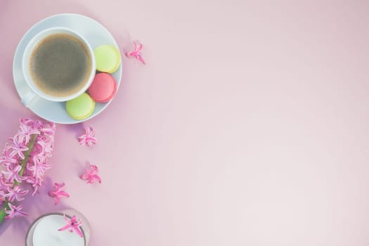 Creative flat lay photo of coffee cup with flowers, candle and macaroons with copy space on pink background minimal style