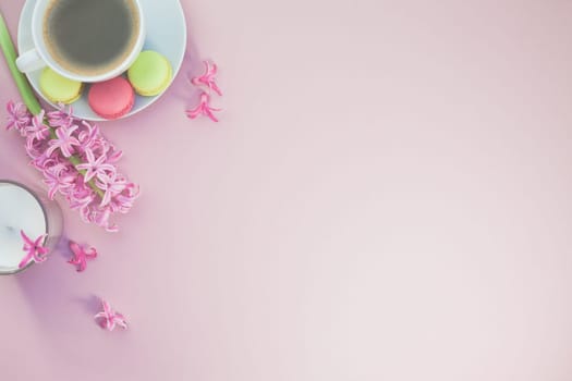 Creative flat lay photo of coffee cup with flowers, candle and macaroons with copy space on pink background minimal style