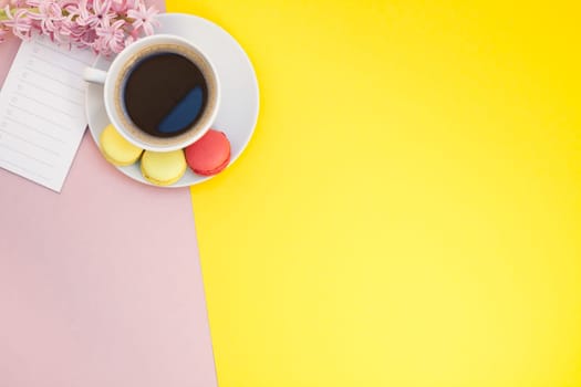 Creative flat lay photo of coffee cup with flowers, candle and macaroons with copy space on pink background minimal style