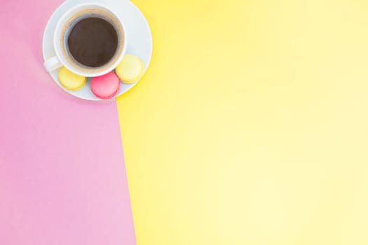 Creative flat lay photo of coffee cup and macaroons with copy space on pink and yellow background minimal style