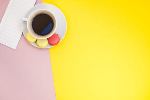 Creative flat lay photo of coffee cup and macaroons and empty list with copy space on pink background minimal style