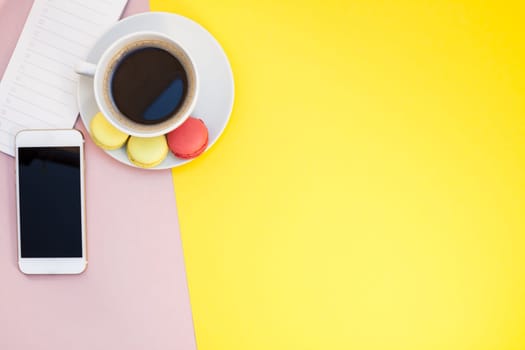 Creative flat lay photo of coffee cup with macaroons and smartphone with empty list with copy space on pink background minimal style