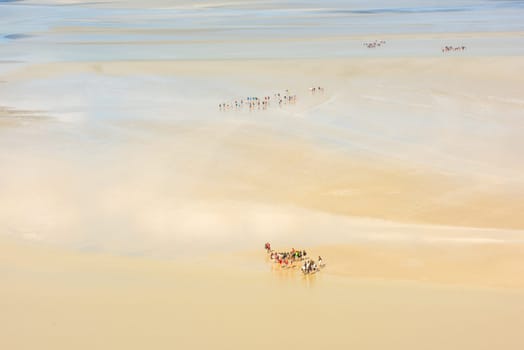 View from walls of Mont Saint Michel on the bay during the low tide with groups of tourists walking. France
