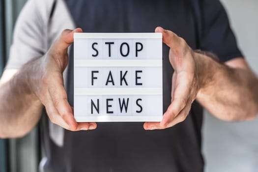Fake news infodemics during Covid-19 pandemic concept. Man hands holding lightbox with text Stop fake news on foreground. People want to know the truth about coronavirus world spread.