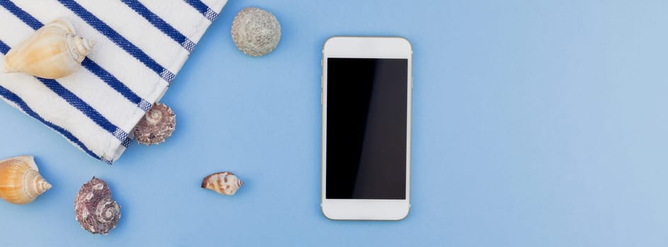 Creative long wide banner flat lay concept of summer travel vacations. Top view of beach towel, seashells, starfish and smartphone on pastel blue background with copy space in minimal style, template