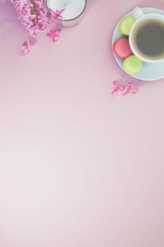 Creative flat lay photo of coffee cup with flowers, candle and macaroons with copy space on pink background minimal style
