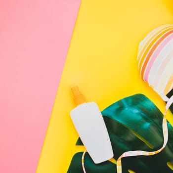 Tropical jungle palm monstera leaves, sunglasses, sunscreen blank bottle mockup and woman's swimsuit top on bright square color paper background. Summer vacations creative flat lay concept template