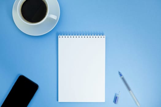 Creative flat lay photo of workspace desk with paper notebook, smartphone, earpieces, pen and coffee with copy space background minimal style