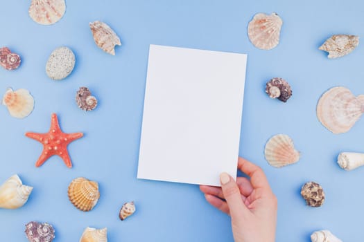Creative flat lay concept of summer travel vacations. Top view of seashells and starfish on pastel blue background with postcard mock up and copy space in minimal style, template for text