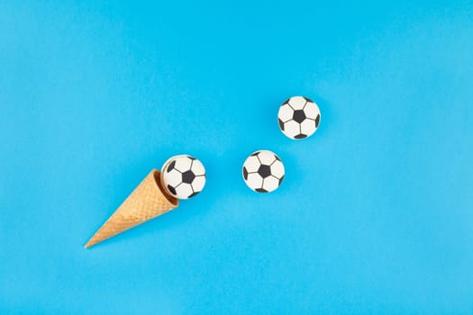 Creative flat lay top view of ice cream waffle cones with soccer balls macarons on bright bold blue background with copy space in minimal style, concept of football games for children birthday