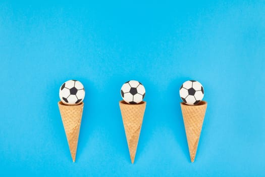 Creative flat lay top view of ice cream waffle cones with soccer balls macarons on bright bold blue background with copy space in minimal style, concept of football games for children birthday