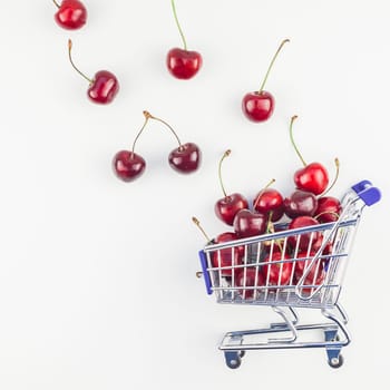 Square image of ripe cherries in a shopping cart with copy space isolated on white background in minimal style. Concept of supermarket or fruit market shopping. Template for your text or design.