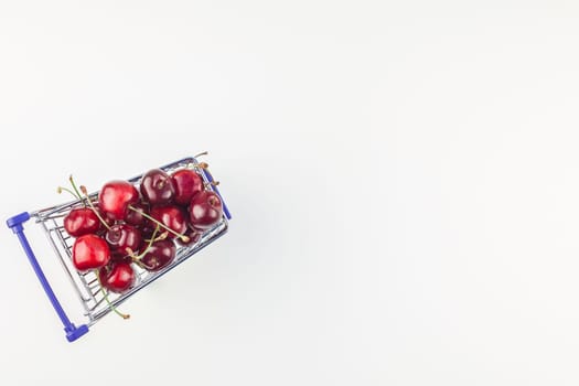 Creative top view of ripe cherries in a shopping cart with copy space isolated on white background in minimal style. Concept of supermarket or fruit market shopping. Template for your text or design.