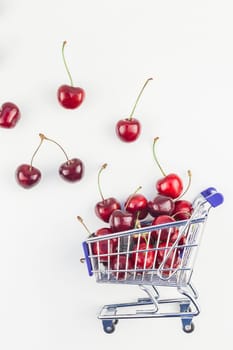 Creative image of ripe cherries in a shopping cart with copy space isolated on white background in minimal style. Concept of supermarket or fruit market shopping. Template for your text or design.