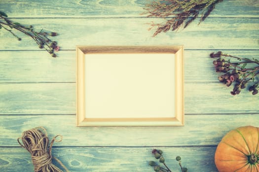 Top view of autumn orange pumpkins and dry flowers with grass thanksgiving background over blue toned wooden table with golden frame mock up and copy space in rustic style, template for text