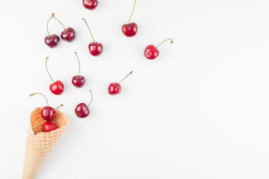 Creative top view of ripe cherries in a waffle cone with copy space isolated on white background in minimal style. Concept of summer fun and healthy eating. Template for your text or design.