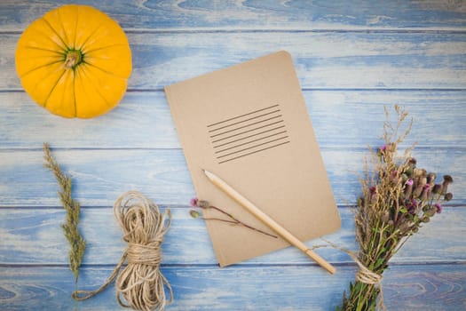 Top view of autumn orange pumpkins and dry flowers with grass thanksgiving background over blue toned wooden table with notebook mock up and copy space in rustic style, template for text