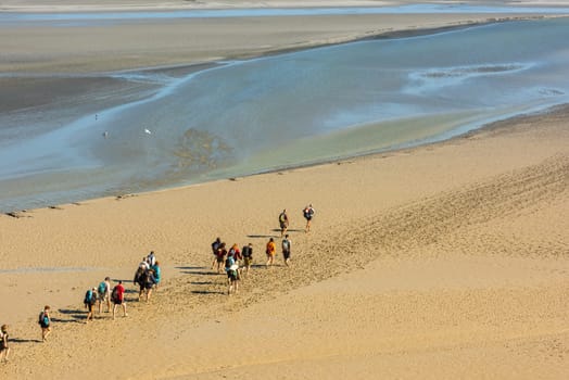 FRANCE, MONT SAINT MICHEL - SEPTEMBER 26: View from walls of Mont Saint Michel on the bay during the low tide with groups of tourists walking. France on September 26, 2015