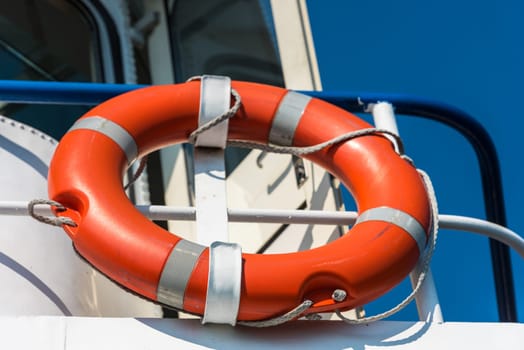 Bright orange lifebuoy on a white yacht side. Blue sky background