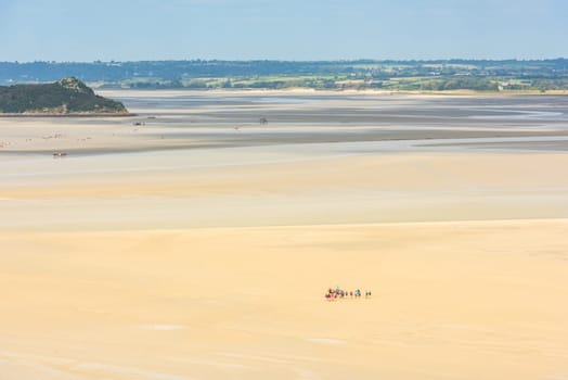 View from walls of Mont Saint Michel on the bay during the low tide with groups of tourists walking. France