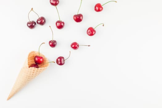 Creative top view of ripe cherries in a waffle cone with copy space isolated on white background in minimal style. Concept of summer fun and healthy eating. Template for your text or design.