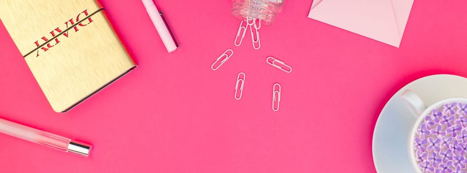 Creative top view flat lay of workspace desk styled design office supplies and cup of tea with copy space on a bright pink color paper long wide banner. Template for feminine blog social media