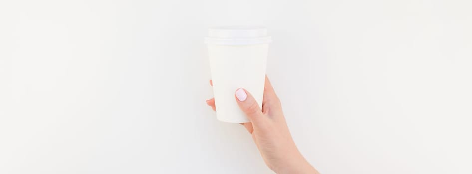 Long wide banner mock up of woman hand holding paper coffee cup with copy space isolated on white background in minimalism style. Template for feminine blog, social media